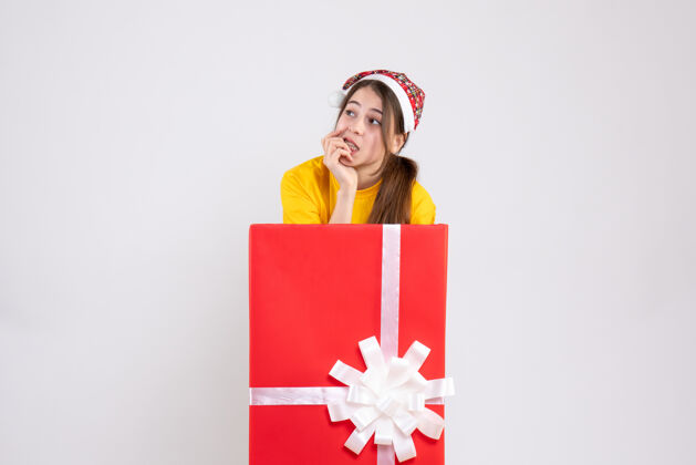 丝带大圣诞礼物后面站着一个戴圣诞帽的女孩人圣诞老人盒子