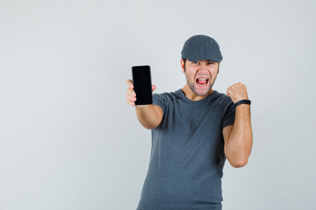 电脑网络摄像头戴着t恤帽拿着手机的年轻男性 看上去很幸福兴奋的小手机速度训练