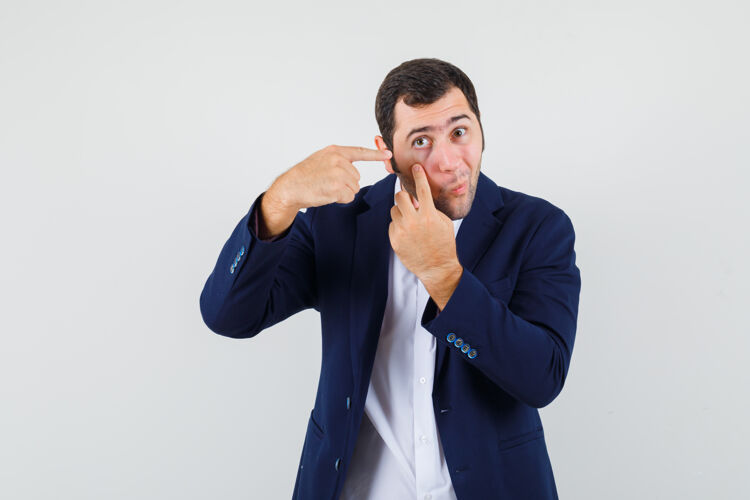 衬衫穿衬衫的年轻男子指着他的眼睛花花公子不寻常姿势