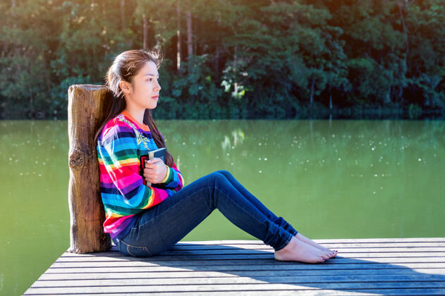 休息一个年轻女孩拿着一本书坐在码头上水河流湖泊