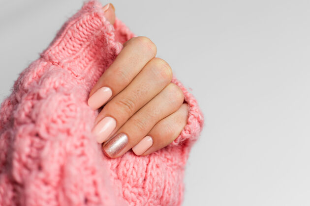 指甲设计漂亮的裸色美甲 一个手指闪亮的金色 在针织粉色羊毛枕头的背景下皮肤美容师手指