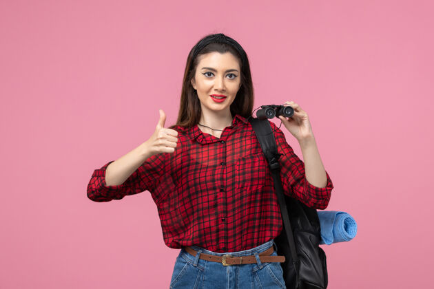衬衫正面图穿红色衬衫的年轻女性用望远镜在粉色背景上拍摄时尚色彩的女人黑发女士年轻女性