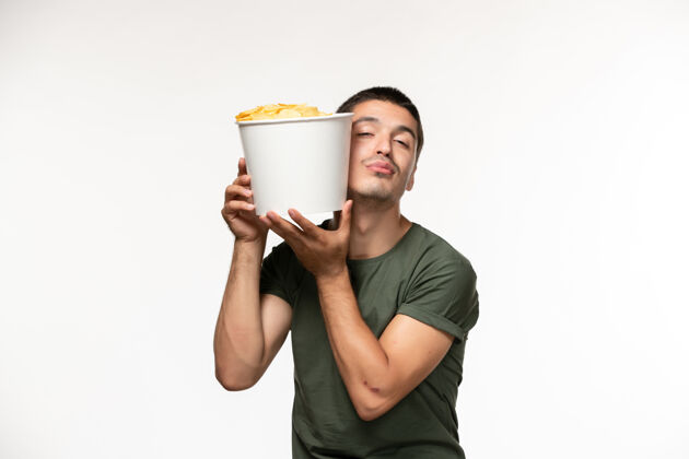 肖像正面图身穿绿色t恤的年轻男子手持土豆cips站在白墙上孤独的人电影视图电影
