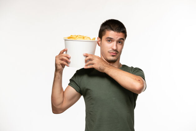 年轻男性正面图身穿绿色t恤的年轻男子手持土豆cips在白墙上的人孤独的电影电影院微笑成人杯子