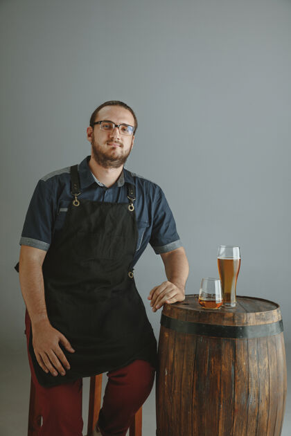 测试自信的年轻男性酿酒师 在灰色的木桶上用玻璃瓶自制啤酒啤酒酒吧成功