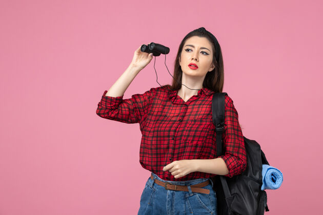 漂亮正面图穿红色衬衫的年轻女性用望远镜在粉色背景上画学生色的女人人脸黑发