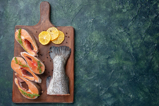 木板新鲜生鱼的俯视图柠檬片绿色胡椒放在木质砧板的右侧深色混合色桌上木头生鱼胡椒粉