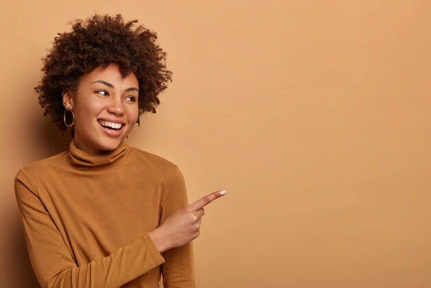 非洲快乐的黑皮肤黑发女人用食指指着旁边的广告或图表 告诉大家非常好的消息 建议有史以来最好的交易 在店里看到最喜欢的产品 穿高领毛衣项目娱乐显示