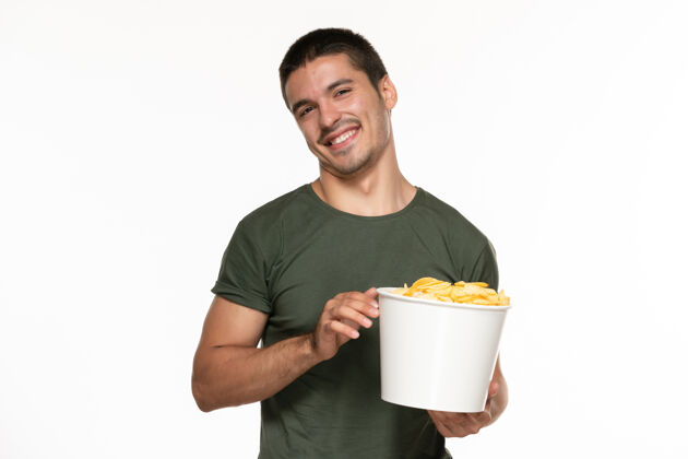 观看正面图身着绿色t恤的年轻男性 手拿着篮子和土豆 微笑着站在白墙上 孤独地享受着电影电影院微笑杯子