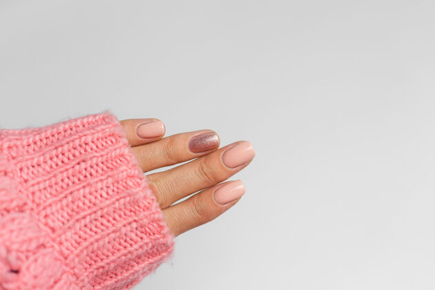 明亮漂亮的裸色美甲 一个手指闪亮的金色 在针织粉色羊毛枕头的背景下美容师指甲设计工艺