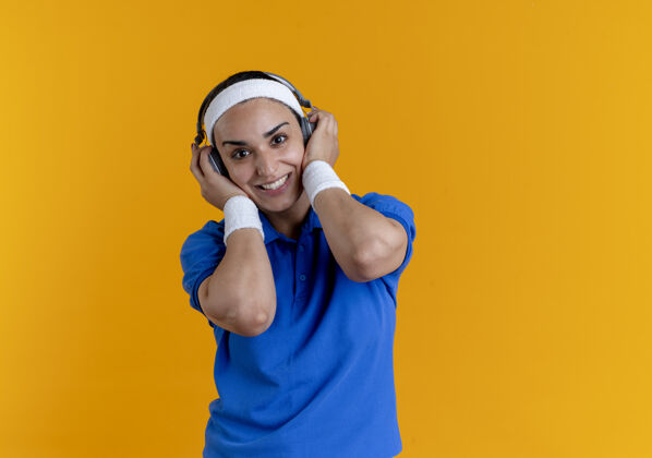 复制年轻微笑的白人运动女性戴着头带和腕带 手持橙色耳机 留有复印空间微笑耳机腕带