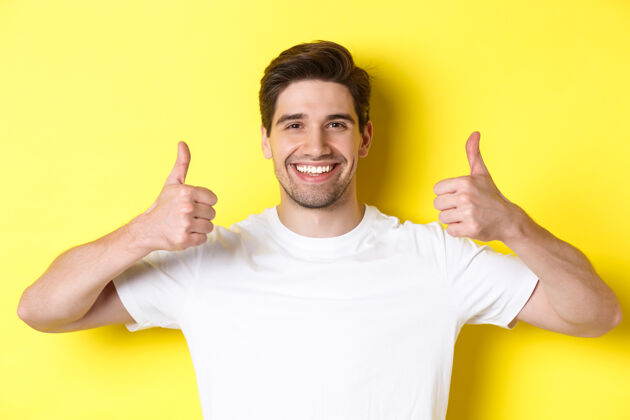 表情帅哥的特写镜头竖起大拇指 表示赞同 满意地微笑 站在黄色背景上时尚站立男人