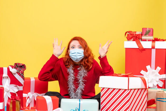 外科面具正面图年轻女子围坐在圣诞礼物与面具上的黄色病毒情感冠状病毒-新年的颜色前面周围面具