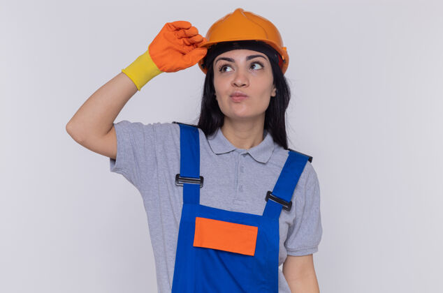 建筑身穿施工制服 头戴安全帽的年轻建筑工人困惑地抬头望着站在白墙上的头盔拼图女人站立