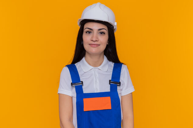 微笑身穿施工制服 头戴安全帽的年轻建筑工人站在橙色的墙上 面带微笑 自信地看着前方自信站立安全