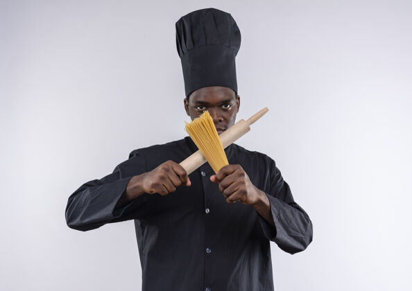 制服年轻自信的非裔美国厨师身着厨师制服 在白色的擀面杖和一堆意大利面上交叉 留有复制空间交叉束空间