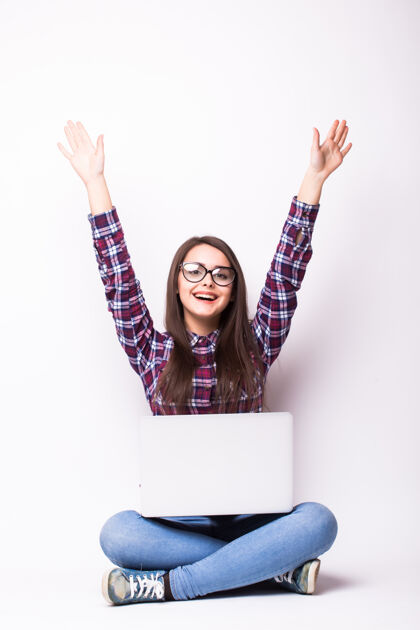 女人一个女人坐在地板上 手里拿着一台笔记本电脑 举起双臂——隔离在白色背景上女性兴奋坐着