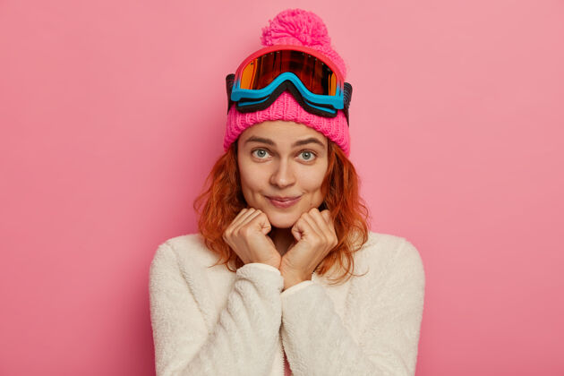 休闲迷人的红发女人戴着暖和的帽子 滑雪镜和白色套头衫毛衣肖像享受