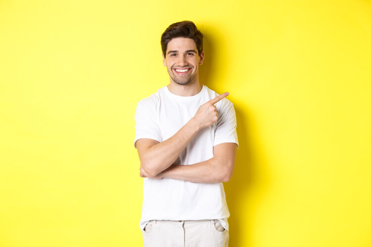 男人有魅力的年轻人用手指指着复制空间 展示横幅或促销优惠 站在黄色背景上的形象秀成人帅