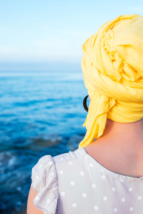 皮肤戴着黄领巾欣赏海景的女性垂直镜头背景感染海洋