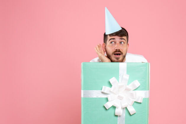 颜色正面图：年轻男性站在礼物盒内浅粉色人类情感圣诞照片睡衣派对年轻男性购物礼物