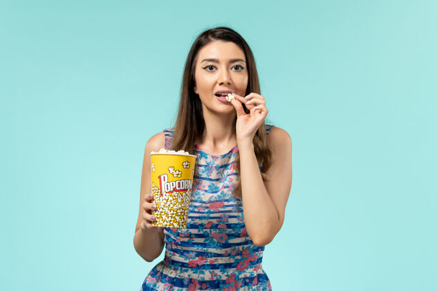 电影正面图年轻女性拿着爆米花包在蓝色的表面上吃电影院剧院封面女郎