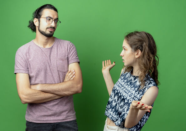 立场一对年轻的男女吵架 女人心烦意乱地站在绿色的墙边和男友说话 双臂交叉 眉头紧锁女人夫妇交叉
