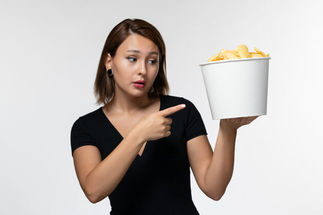 土豆正面图：身穿黑色衬衫的年轻女性手持薯片 在白色桌子上摆姿势女士孤独电影
