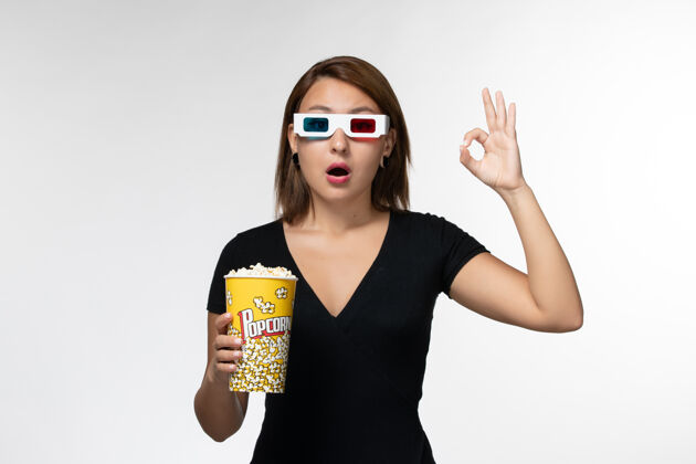 电影正面图年轻女性戴着d型太阳镜拿着爆米花包 在浅白的表面上看电影包装电影院电影