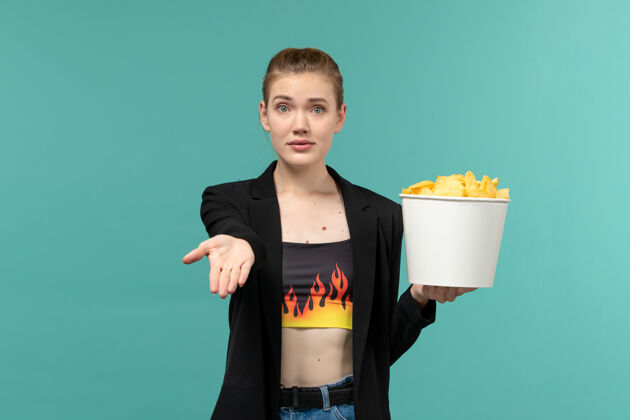 员工正面图：年轻的女性拿着薯片在蓝色的水面上看电影土豆年轻的女性剧院