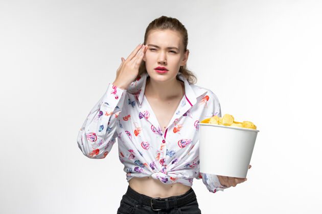 前面前视图年轻的女性拿着土豆片篮子在浅白色的表面上看电影年轻女性电影土豆