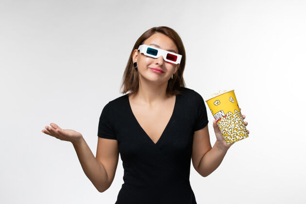 孤独正面图戴着d型太阳镜拿着爆米花的年轻女性在浅白的表面上看电影年轻女性性感电影院