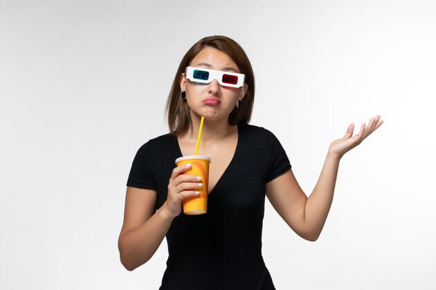 性感正面图：戴着d墨镜拿着苏打水的年轻女性站在白色的表面上电影院太阳镜电影