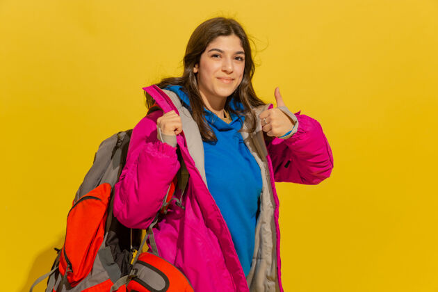 女人黄色摄影棚墙上 一个带着包和望远镜的快乐的年轻旅游女孩的画像手人旅游者