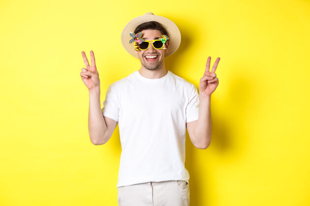 节日旅游和生活方式的概念快乐的男人享受旅行 戴着夏天的帽子和太阳镜 与和平标志合影 黄色背景模特男人黄色