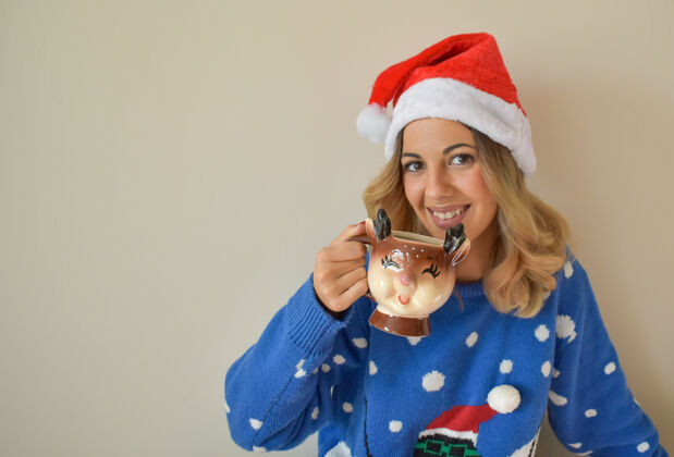 杯子美丽的年轻白人女性 穿着可爱的蓝色圣诞套装 戴着圣诞帽 喝着热巧克力针织季节毛衣