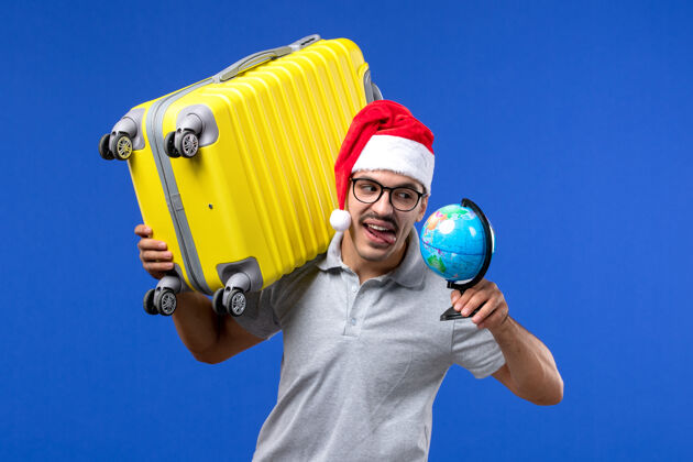 圣诞节正面图年轻男子背着黄包上蓝墙飞机度假旅行男运动肖像气球