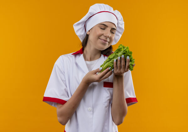 厨师穿着厨师制服的年轻快乐的白人厨师女孩抱着并假装闻到了隔离在橙色空间里的沙拉味空间烹饪复制