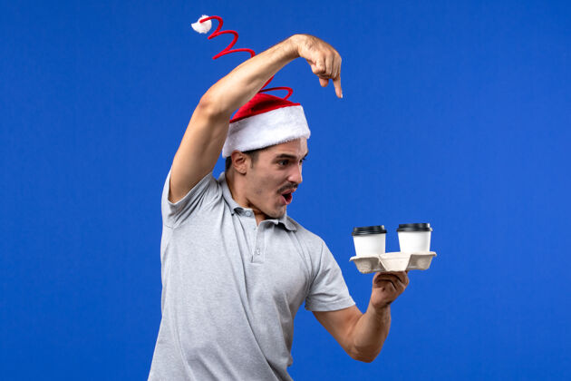 帅哥正面图年轻男性拿着咖啡杯在蓝色的墙上情感人类咖啡蓝色男人圣诞节杯子