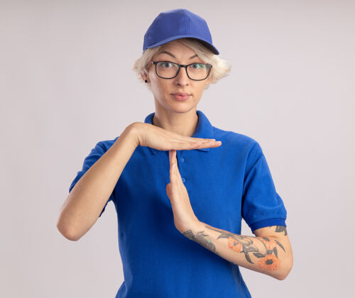 手势身穿蓝色制服 头戴鸭舌帽 表情严肃的年轻女送货员站在白墙上 做着暂停的手势分娩年轻帽子