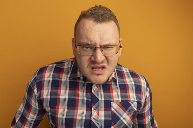 生气一个戴着眼镜 穿着格子衬衫 满脸怒容的男人站在橙色的墙上站起来男人检查