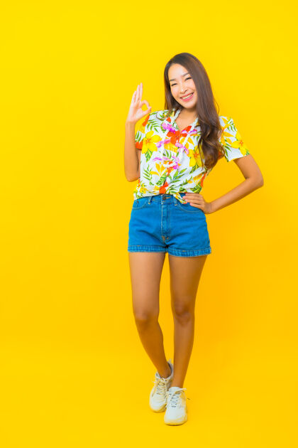 女人美丽的亚洲年轻女子身穿五颜六色的衬衫 在黄色的墙上做着“好”的手势水庆祝季节