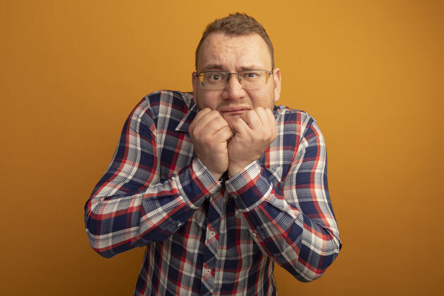 检查一个戴着眼镜 穿着格子衬衫的男人站在橙色的墙上 紧张得咬指甲站着男人咬