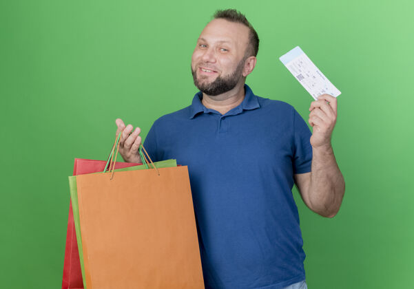 成人微笑的成年斯拉夫人拿着购物袋和机票孤立在绿墙上斯拉夫人机票购物