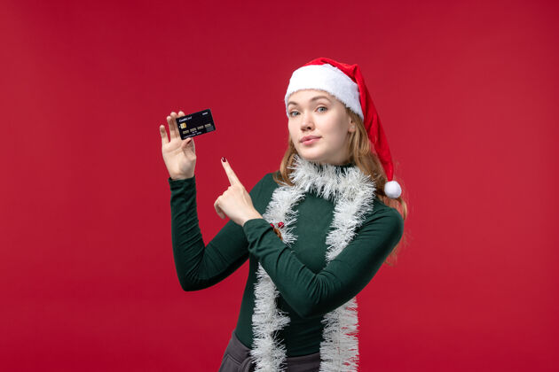 银行正面图年轻女性手持红色背景的黑色银行卡人年轻女性视图