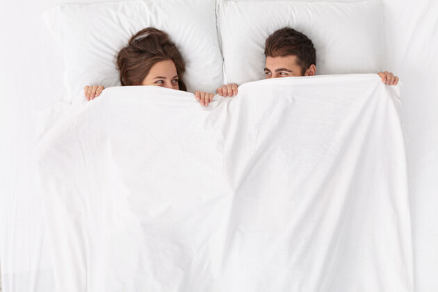 婚礼特写这对躺在床上白毯子下的夫妇隐藏在一起快乐