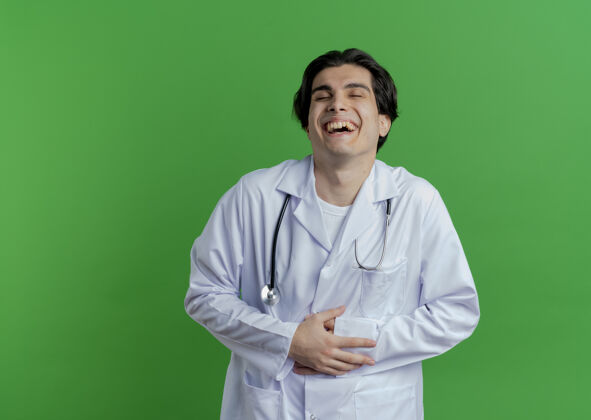 抱着年轻的男医生穿着医用长袍和听诊器抱着肚子笑着闭着眼睛隔离在有复印空间的墙上男性肚子年轻