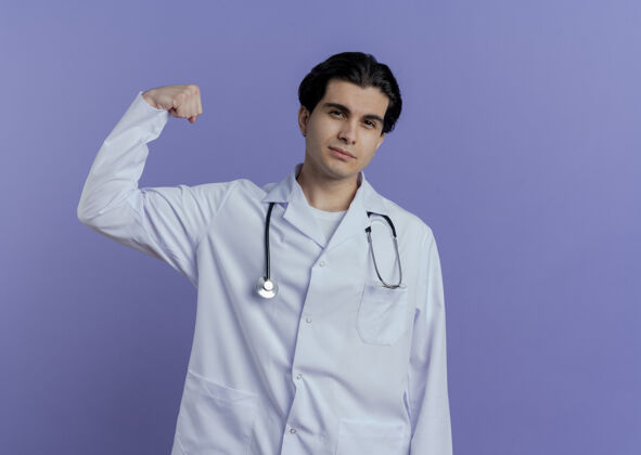 男性自信的年轻男医生穿着医用长袍和听诊器 做着强烈的手势 隔离在紫色的墙上 留着复印空间手势听诊器年轻