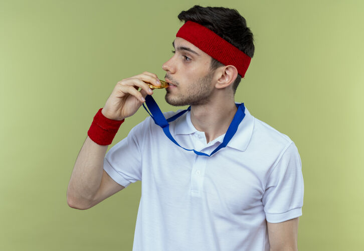 绿戴着头巾 脖子上戴着金牌 咬着奖牌的年轻运动型男子 看上去自信满满头带站咬