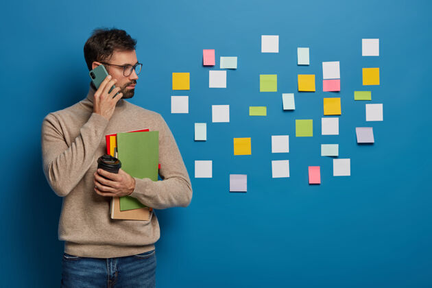 水平白种人有创造性的方法来组织工作 在墙上留下五颜六色的贴纸 通过智能手机与合作伙伴讨论工作日程手机手机男性